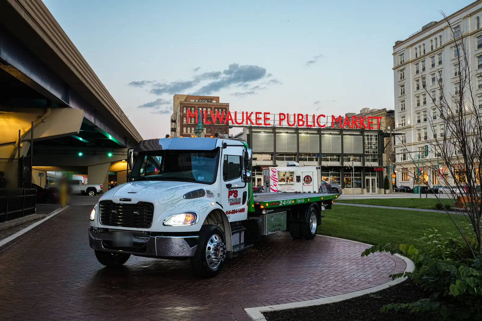Grúa de plataforma Freightliner de PS Towing frente al letrero del Milwaukee Public Market al atardecer